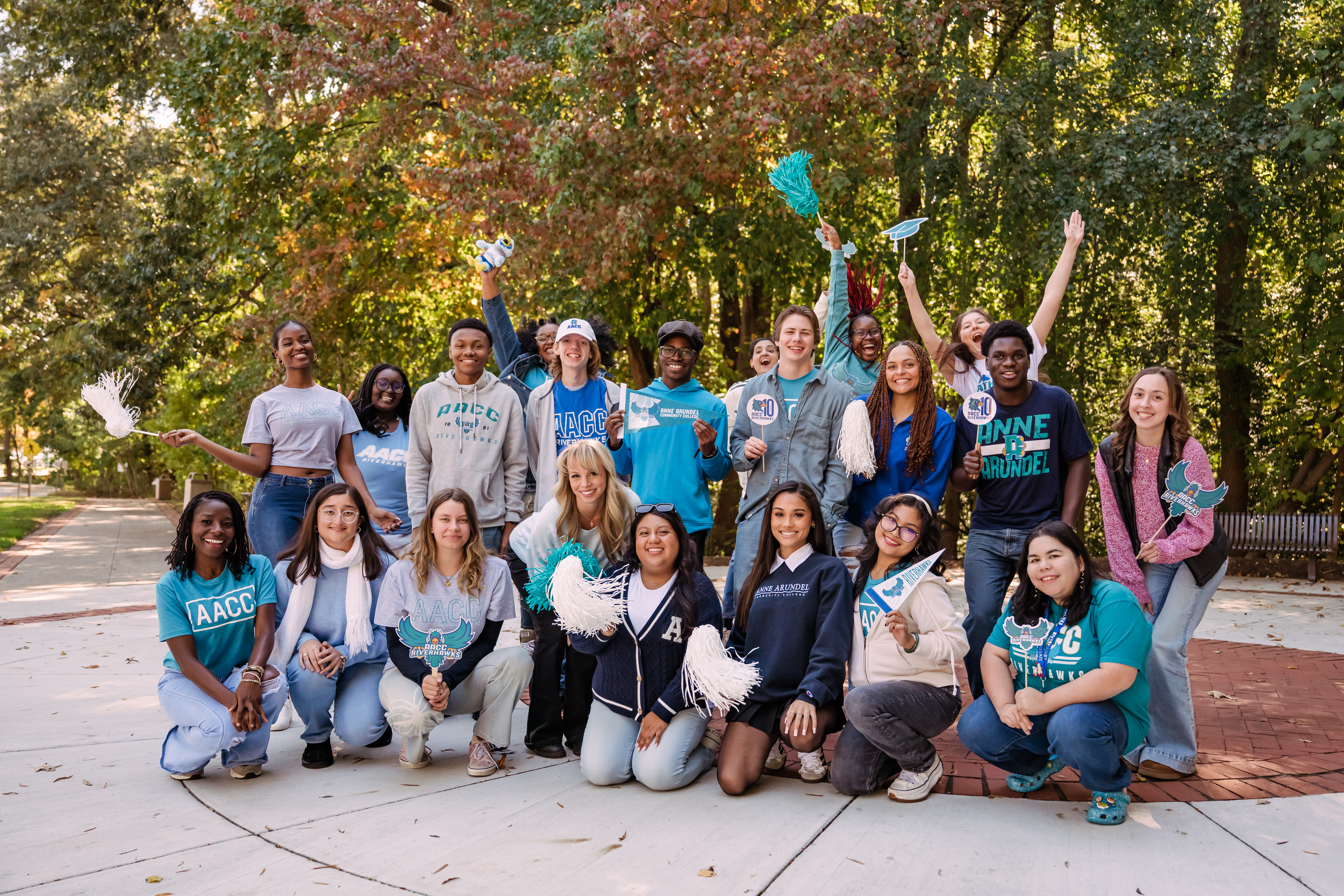 a group of AACC students stand underneath a set of trees on campus, smiling and proudly wearing their AACC spirit clothing.
